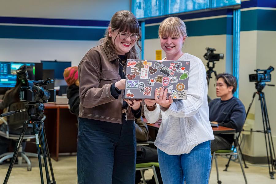 Two students inside the media lab smile while watching a video on their laptop