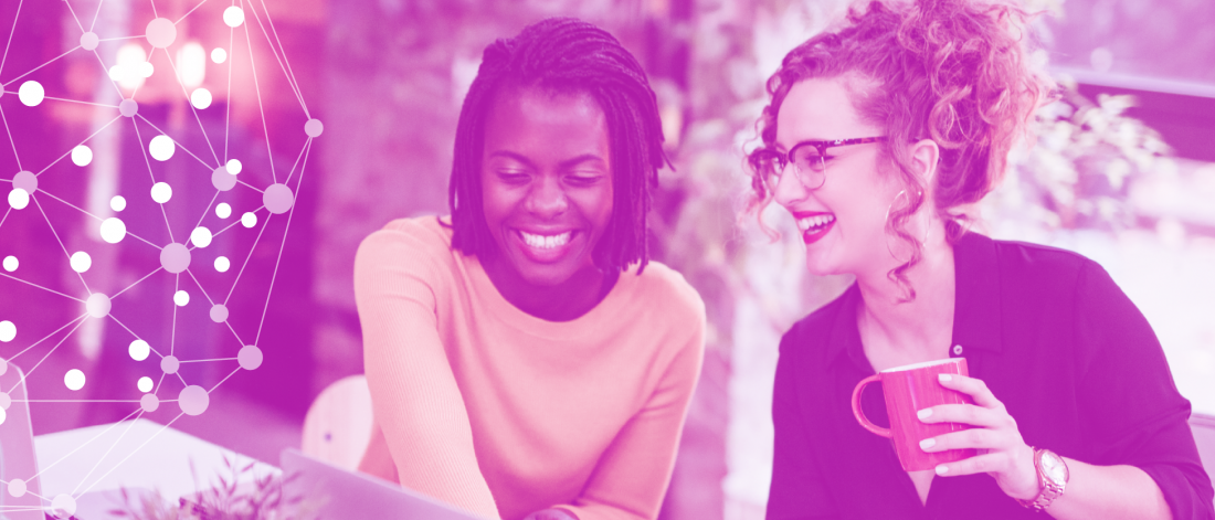Two women sitting a table looking at a computer.
