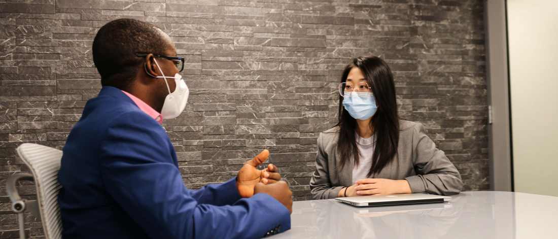 An Asper staff member and finance student sit in a grey boardroom talking at the Asper School of Business Drake Centre.