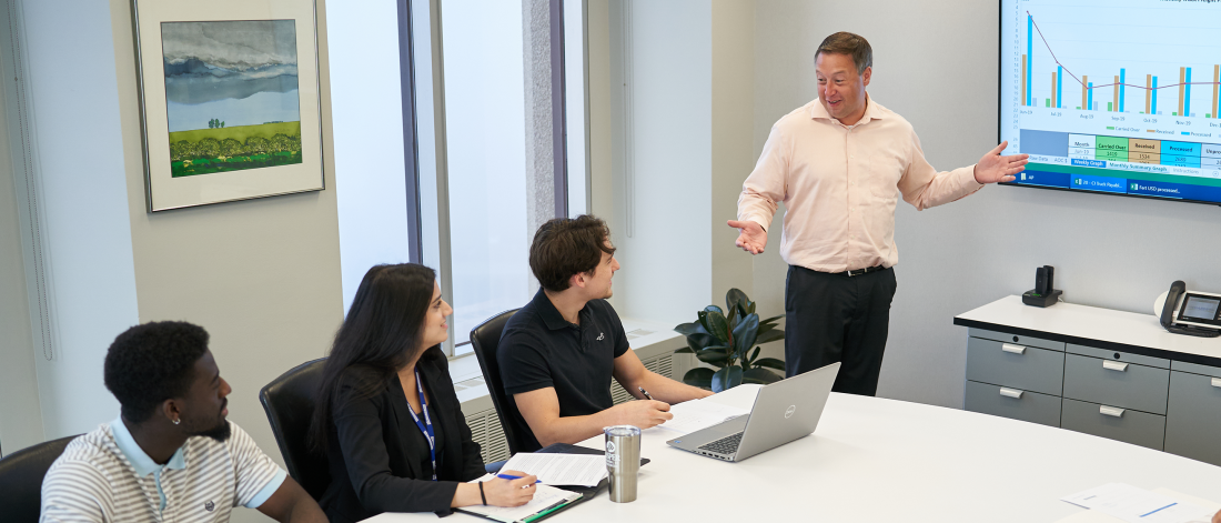 Employer presenting a powerpoint to co-op students in a boardroom.