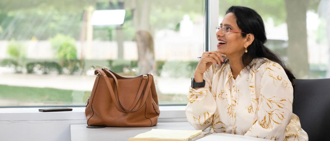 Woman sitting a desk with a purse, smiling. Wearing a watch and blouse.