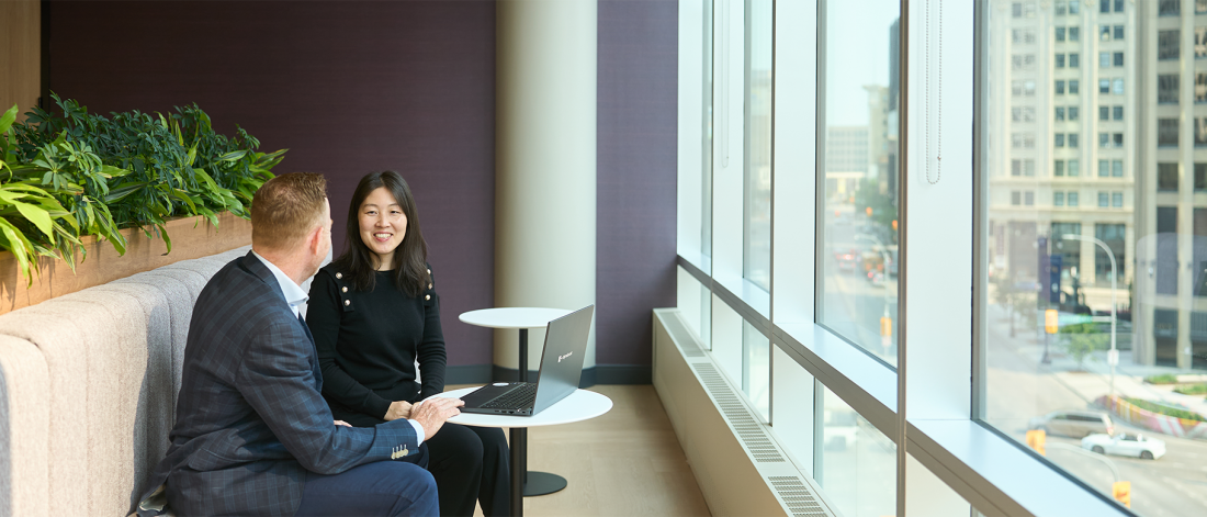 Two people sitting at a small table working over a laptop.
