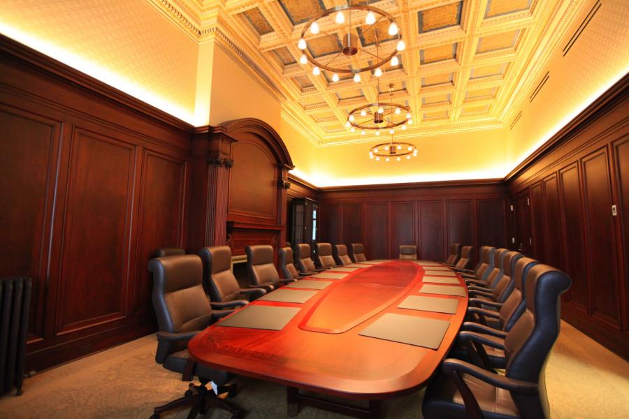 A large oval shaped table surrounded by tall office chairs fills a large wood walled room with tall ceilings.