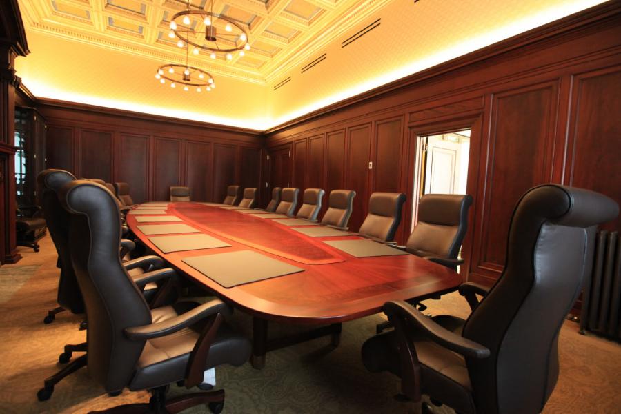 A large boardroom with a long  oval shaped table lined with black office chairs.