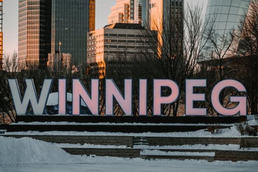 Large sign displaying the word Winnipeg in front of an urban landscape.