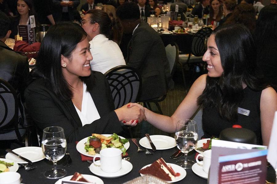 Two women shaking hands and smiling at a dinner table.