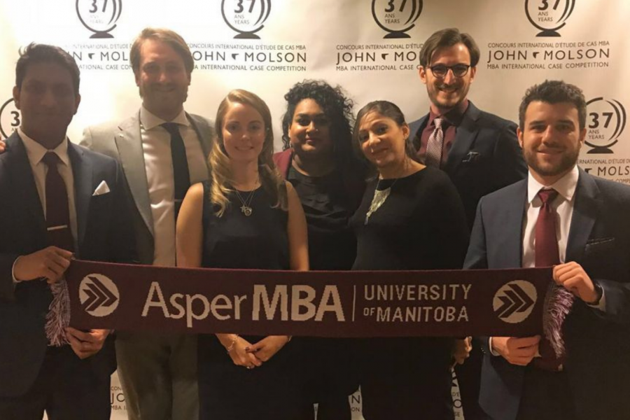 a group of MBA students and coaches posing in front of a white background while holding a red Asper scarf