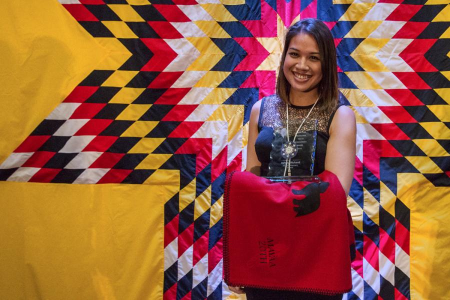 Alumna, Ashley Richard, in front of a star blanket, smiling, holding a red blanket.