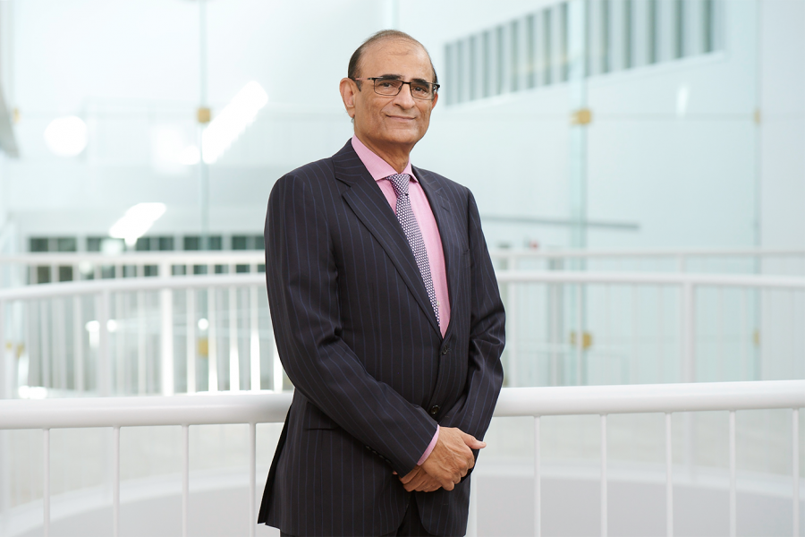 Rakesh Mittoo, professor at the Asper School of Business, wearing a black suit and pink shirt, smiling.