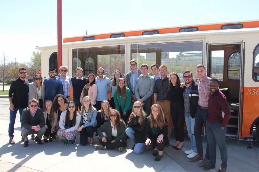 A group of people standing in front of an orange trolley.
