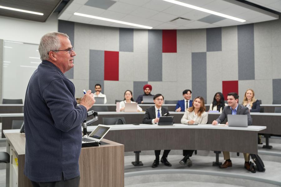 Professor standing at the front of a classroom speaking to a group of students