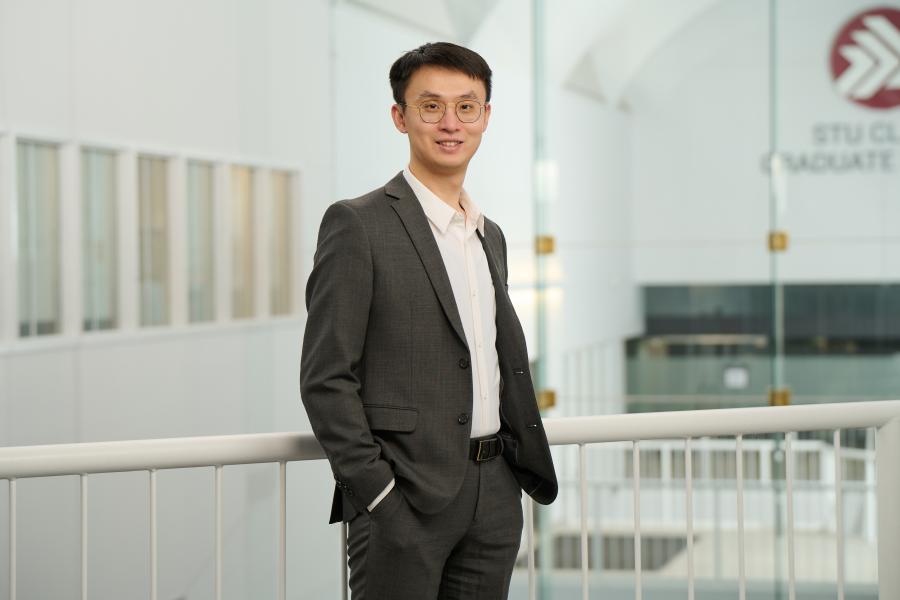 Man with glasses and suit, smiling at camera with hands in pocket.