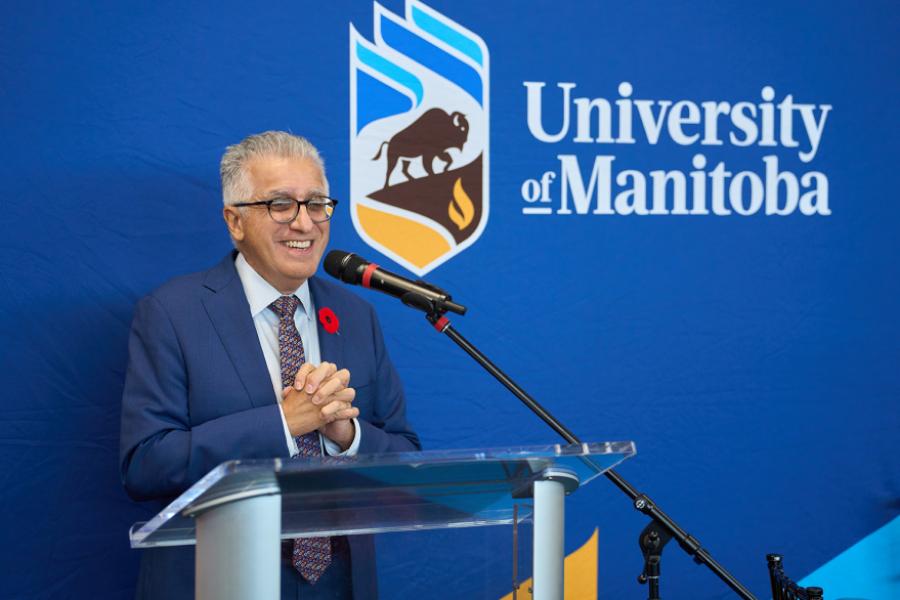 U Manitoba President Michael Benarroch wearing a suit standing in front of a podium speaking.