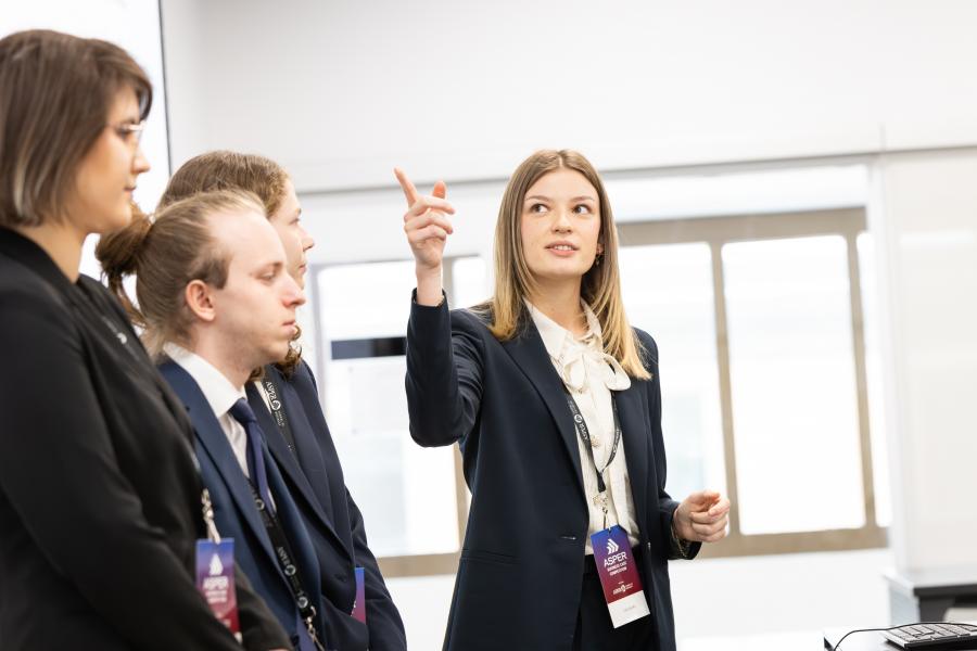 A woman giving a presentation points towards the screen as she speaks with her team beside her.