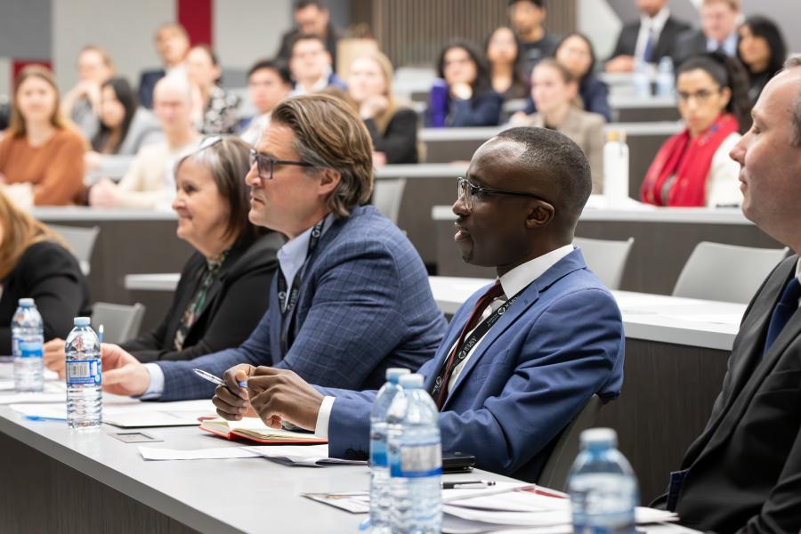 A group of judges watches a presentation with an audience behind them.