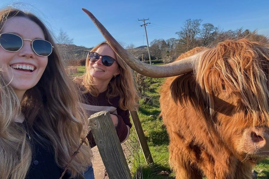 Two young women pose beside a Highland cow