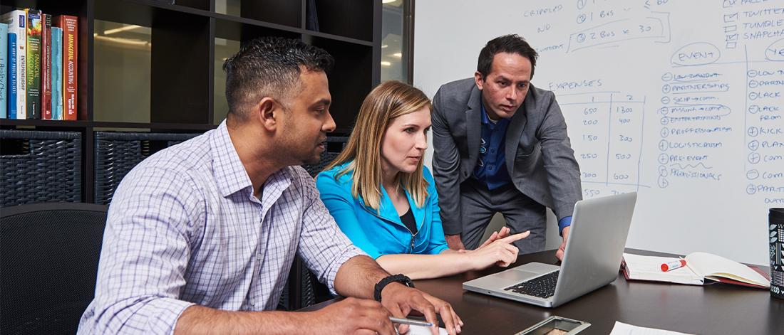 Three UM staffs looking at a laptop.