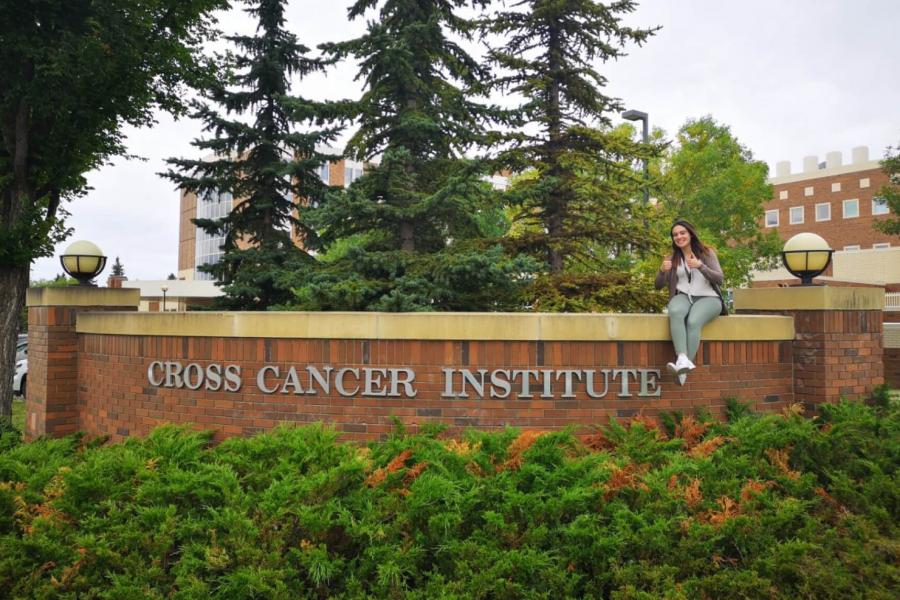 Jennifer Simone sitting on the outdoor Cross Cancer Institute welcome sign.