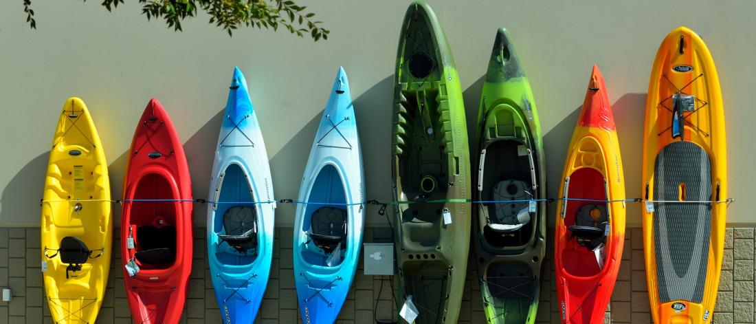 Different coloured kayaks lined up against a wall.