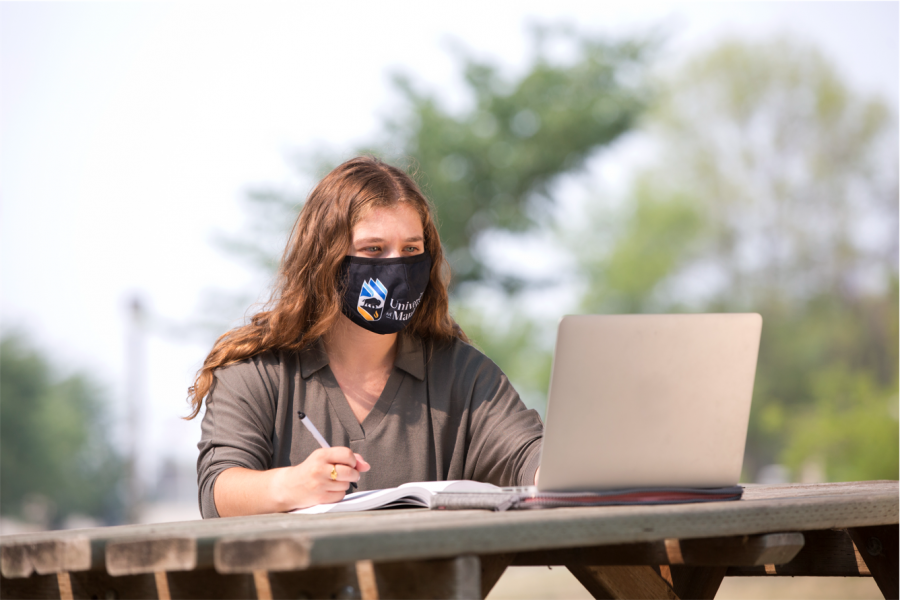 A student looks at a laptop wearing a mask on campus