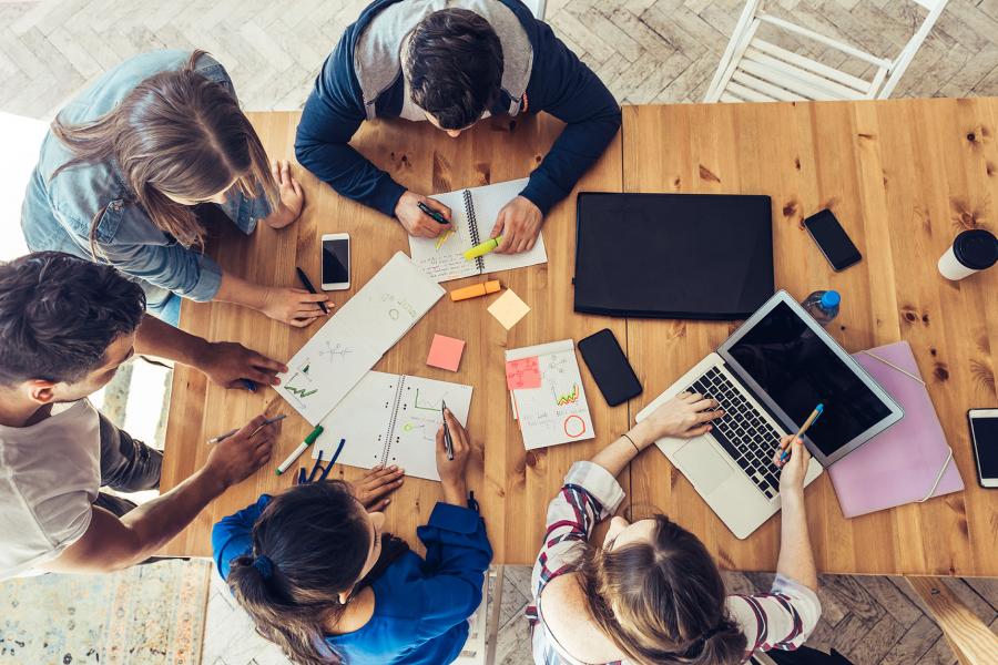 A group of people working on a group project at a wooden table.