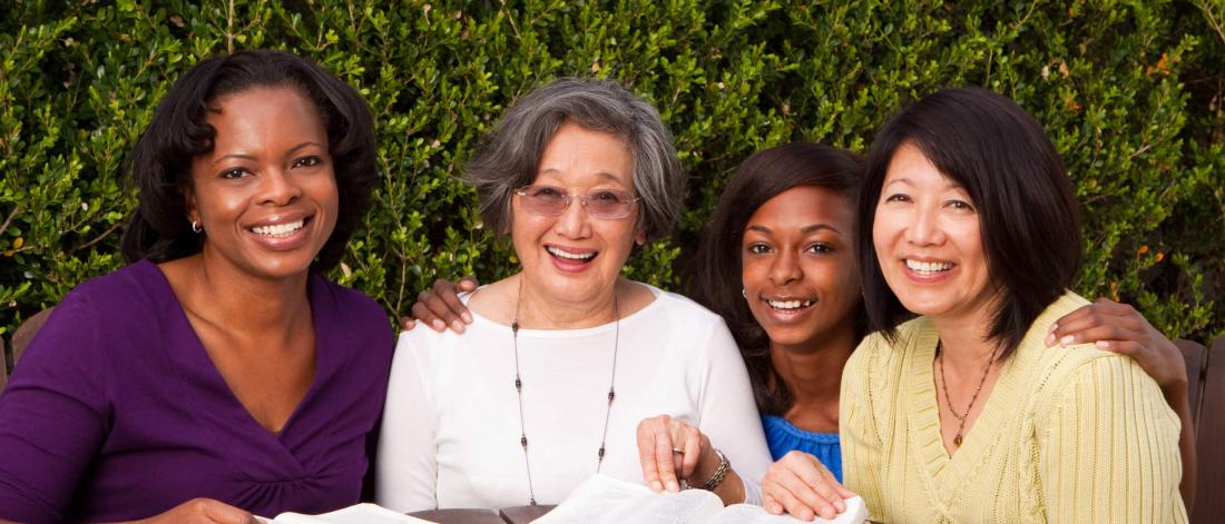 A diverse group of four women of varying ages are smiling and seated at a table.