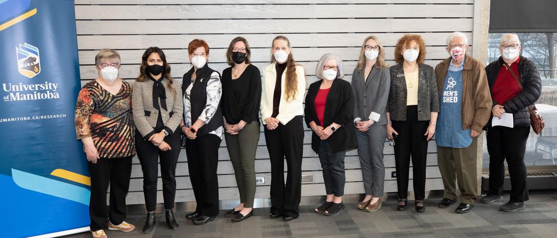 Nine members of the Manitoba Seniors Coalition and senior organizations pose for a photo with the Honourable Kamal Khera (second from left) and Director Dr. Porter (sixth from left) beside the University of Manitoba banner.