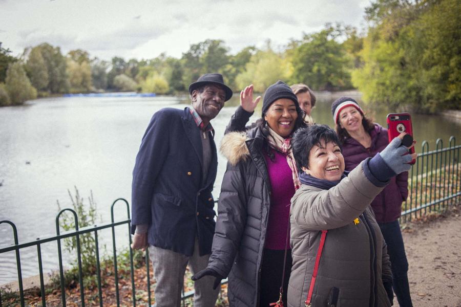 A group of older adults take a group selfie while walking outdoors in a park.