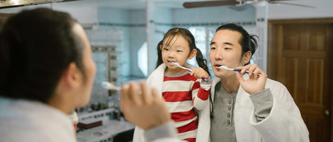 Father and daughter brushing their teeth.
