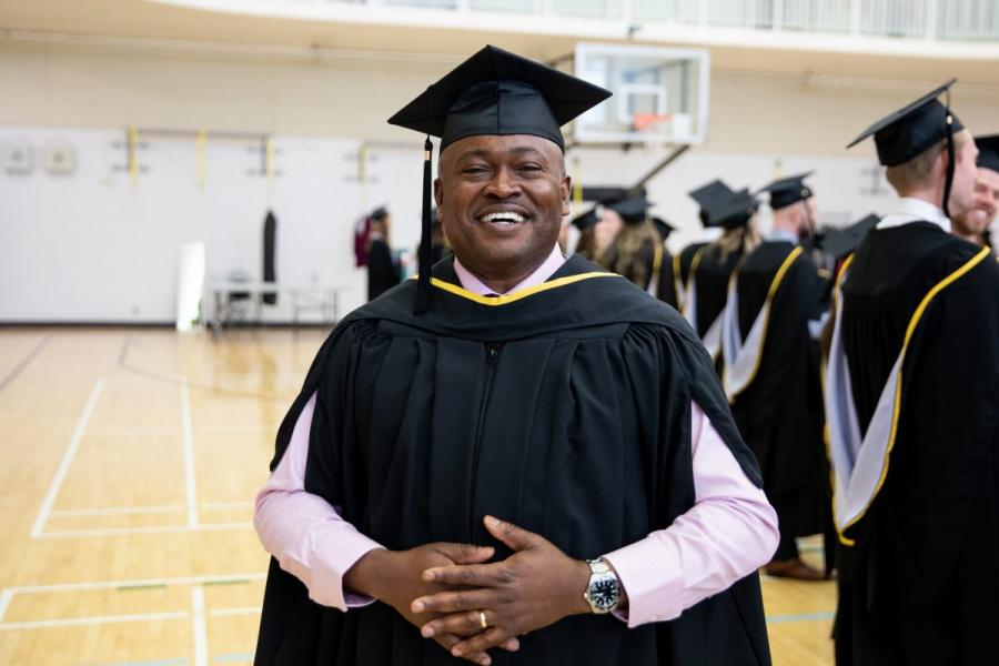 A smiling graduate in a cap and gown, at convocation.