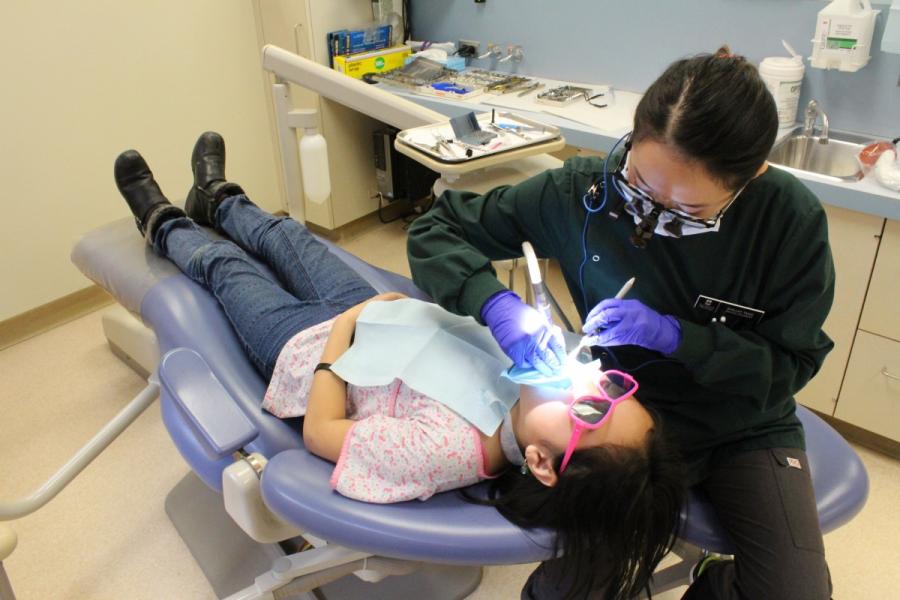 A dentistry student treating a young patient who is laying in a dentists chair.