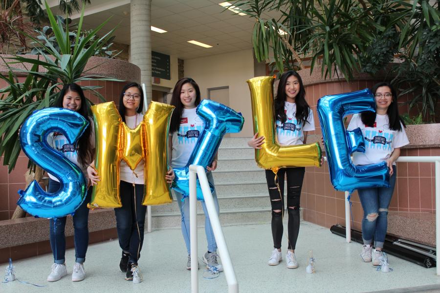 Five people each holding a letter shaped balloon spelling out smile.