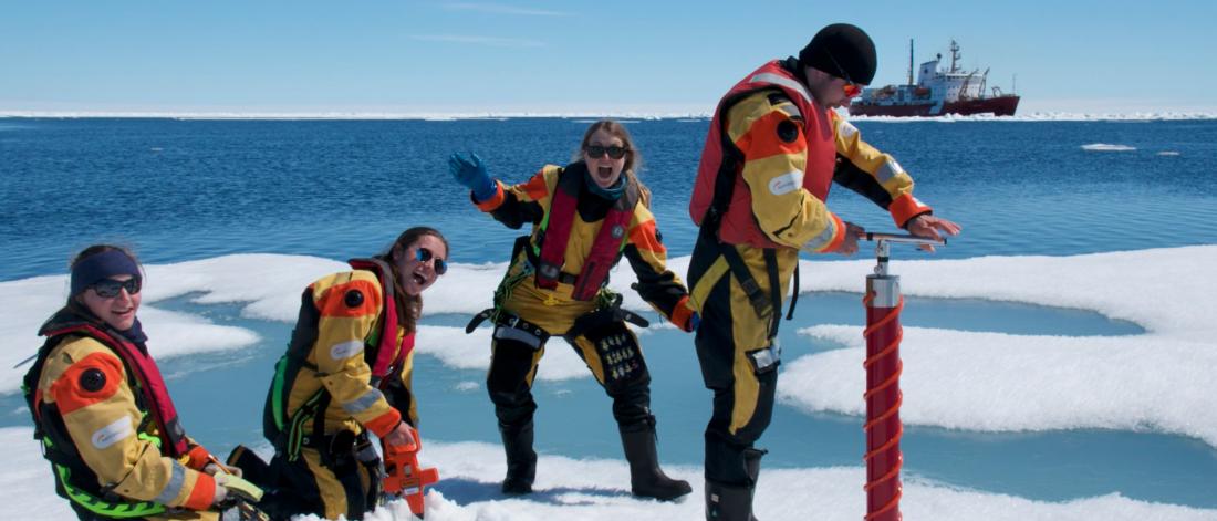 Researchers smiling and enjoying their time on the sea ice as one of them cores the ice