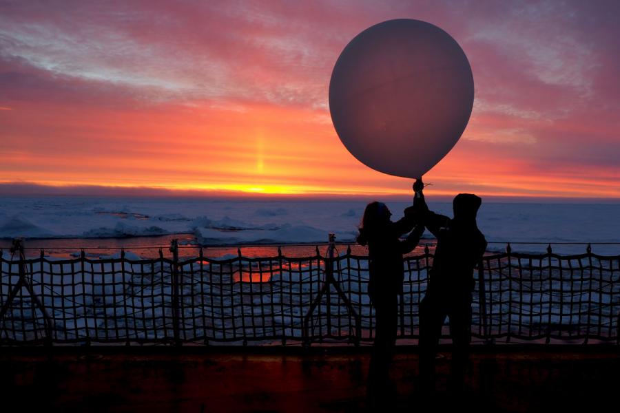two researchers launching a balloon off a boat at sunrise.