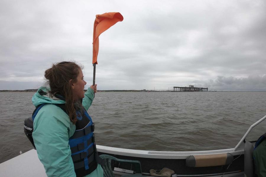 Emma Ausen holding an orange flag on a boat.