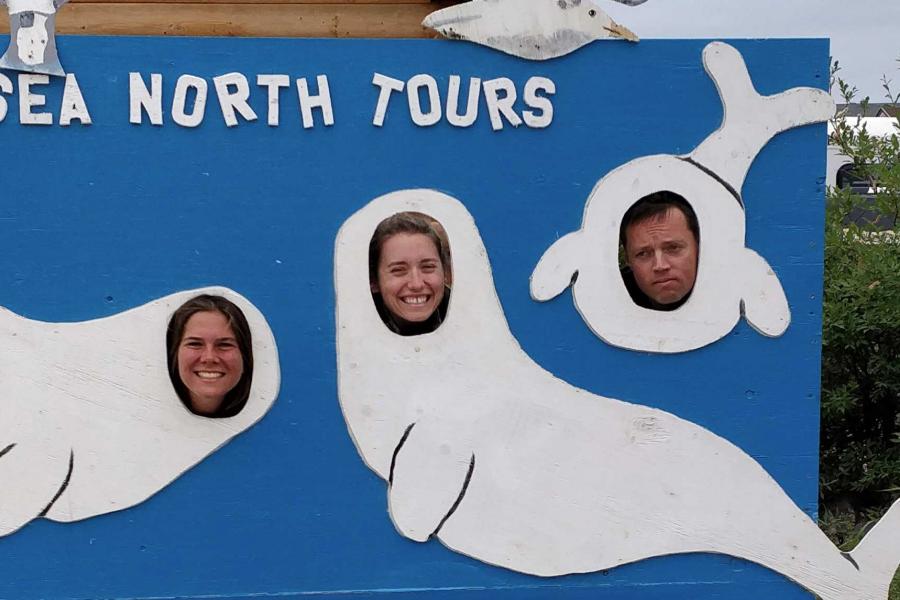 Emma Ausen and fellow researchers poke their faces through a carnival cutout of three belugas.