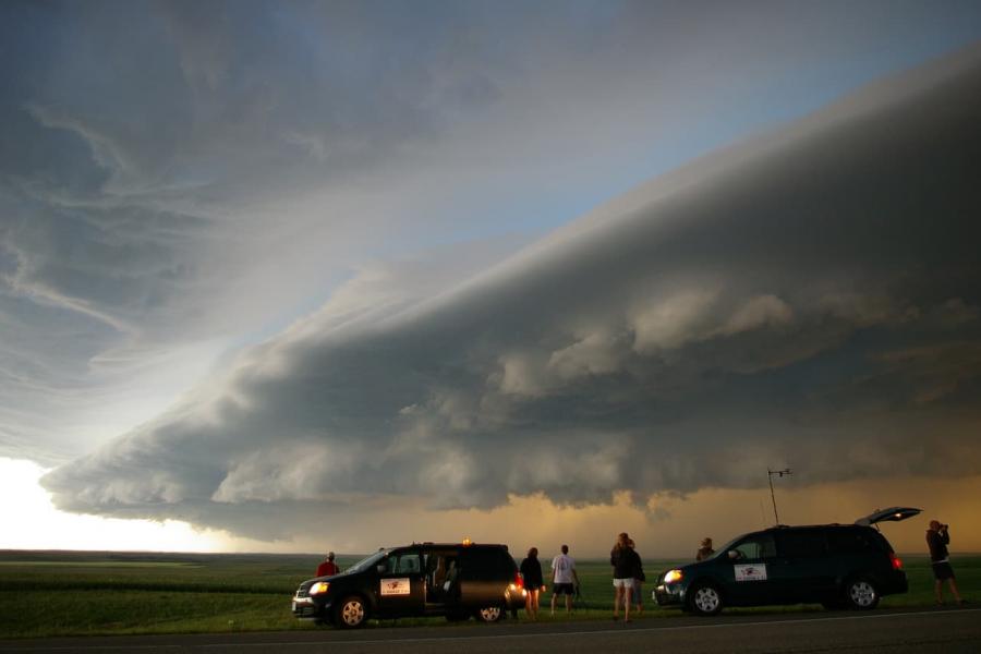 Students stand outside two vans observing storm clouds