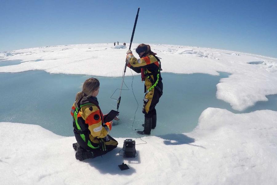 two researchers use equipment on sea ice.