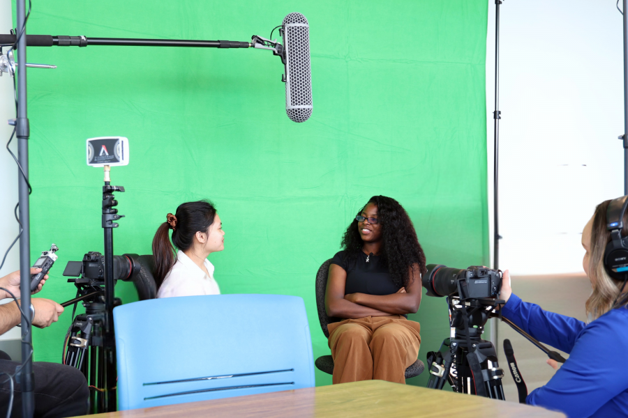 two female students sitting in front of green screen