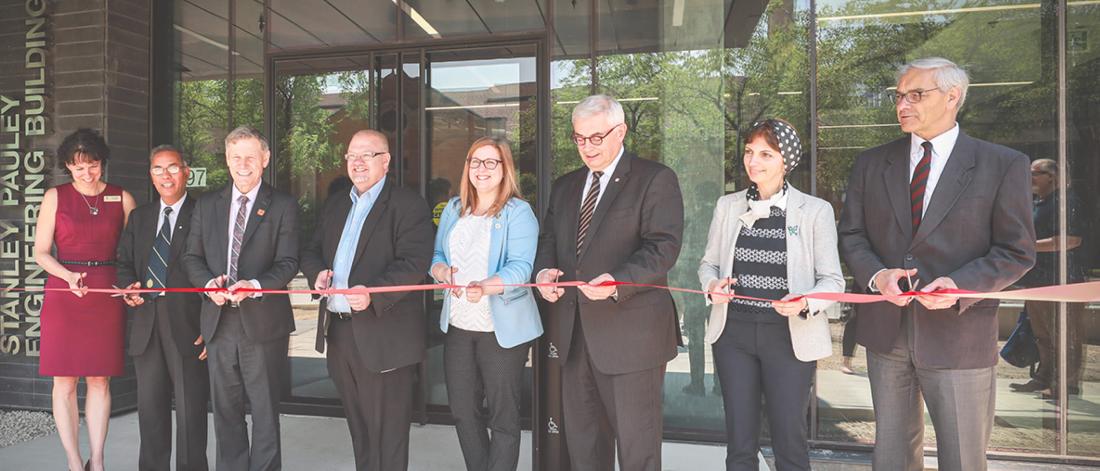 A group of people gather together to cut a red ribbon at the opening for the Stanley Pauley Engineering building.