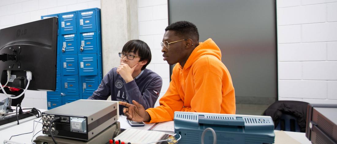 Two engineering students sit at a desk and work together at a computer.