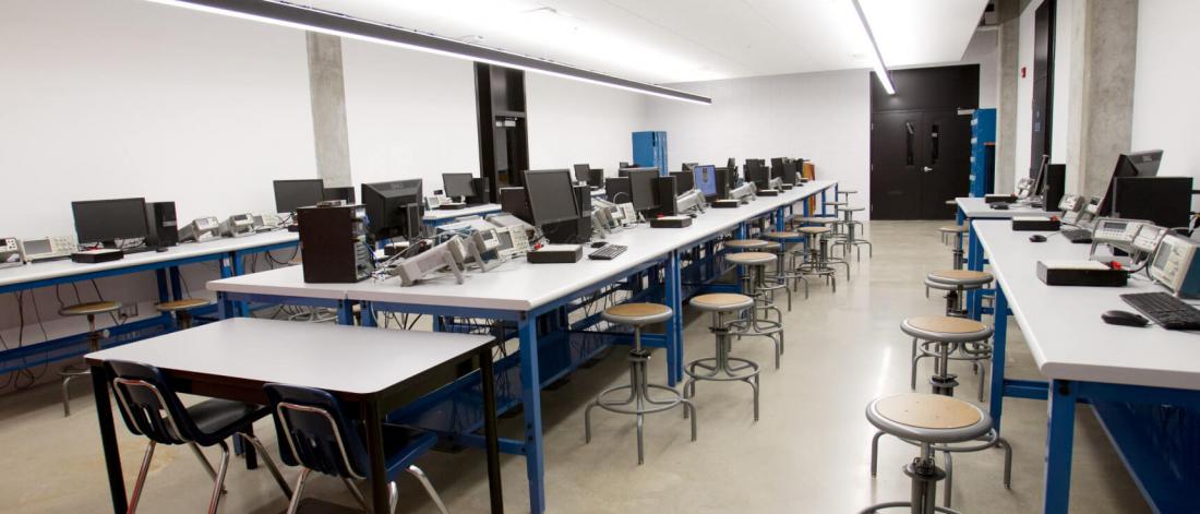A classroom with three rows of computer engineering work stations. 