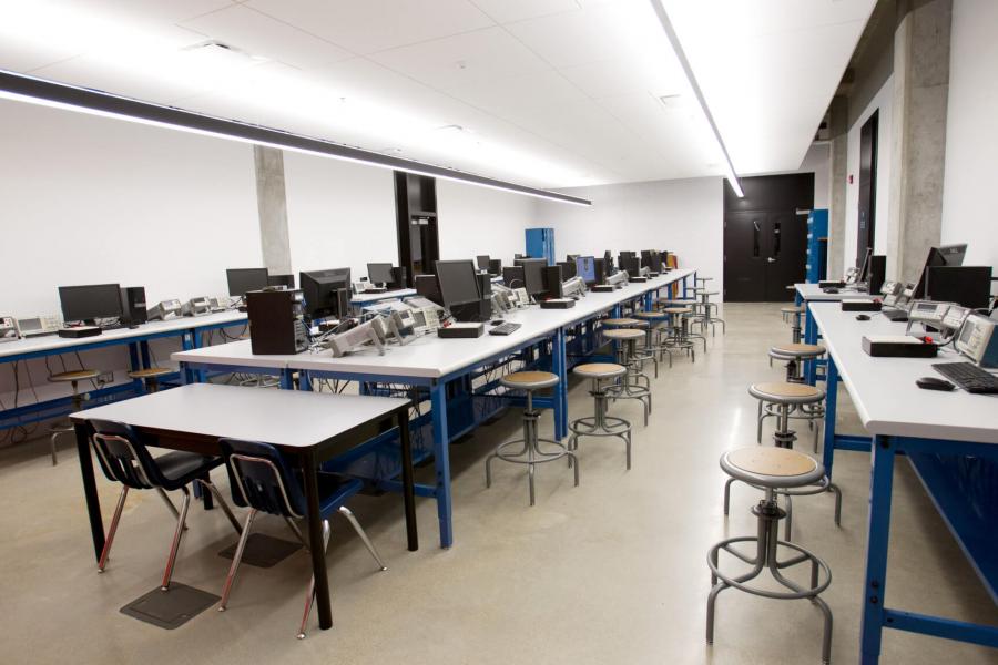 A classroom with three rows of computer engineering work stations. 