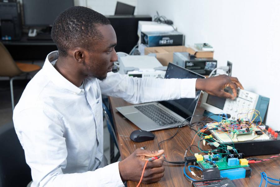 An engineering students sits at a desk while working with computer engineering equipment.