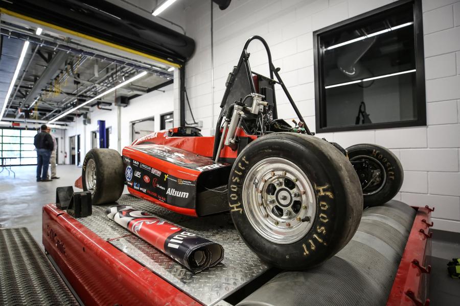 A formula one style race car sits on a lift in a work space inside the Price Innovation Centre