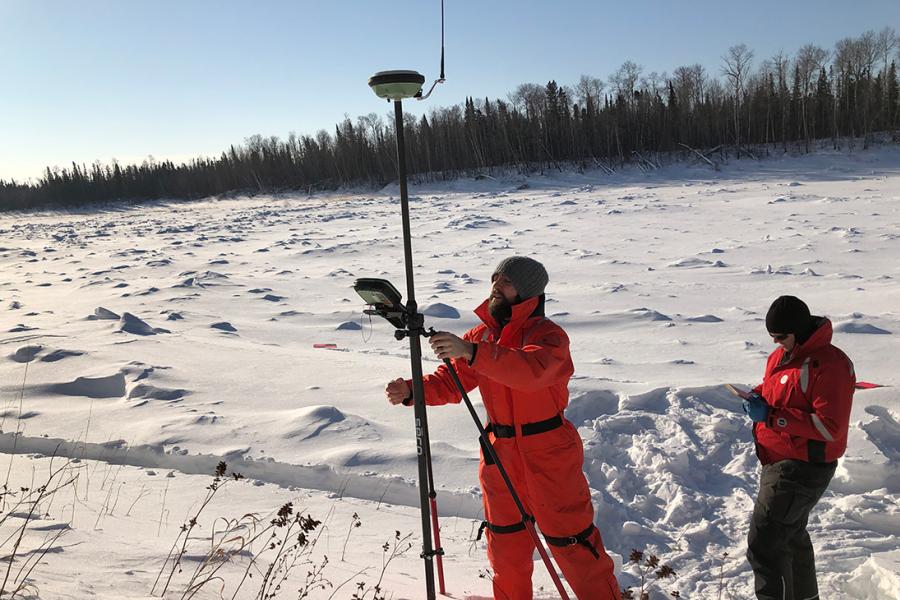 Outside on a sunny winter day, two civil engineering students run land surveys