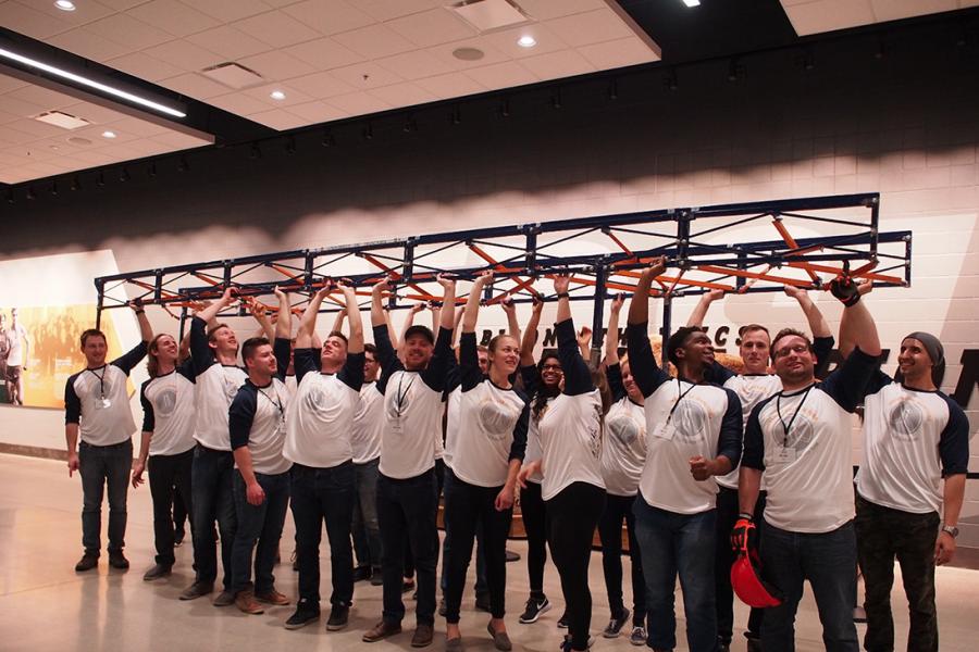 The steel bridge design team (20 member group) holds their build over their heads while posing for the camera