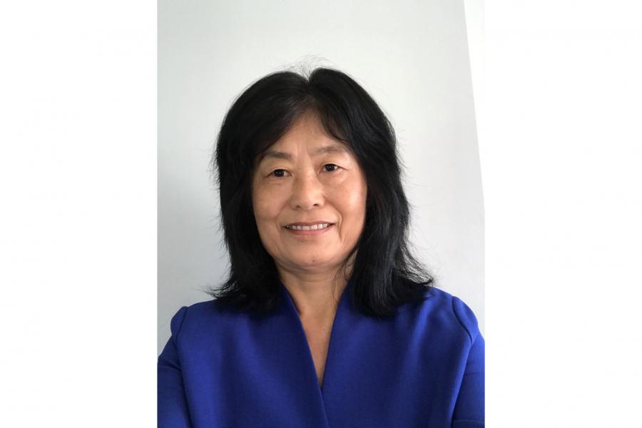Ying Chen stands smiling and posing for the camera against a plain background. 