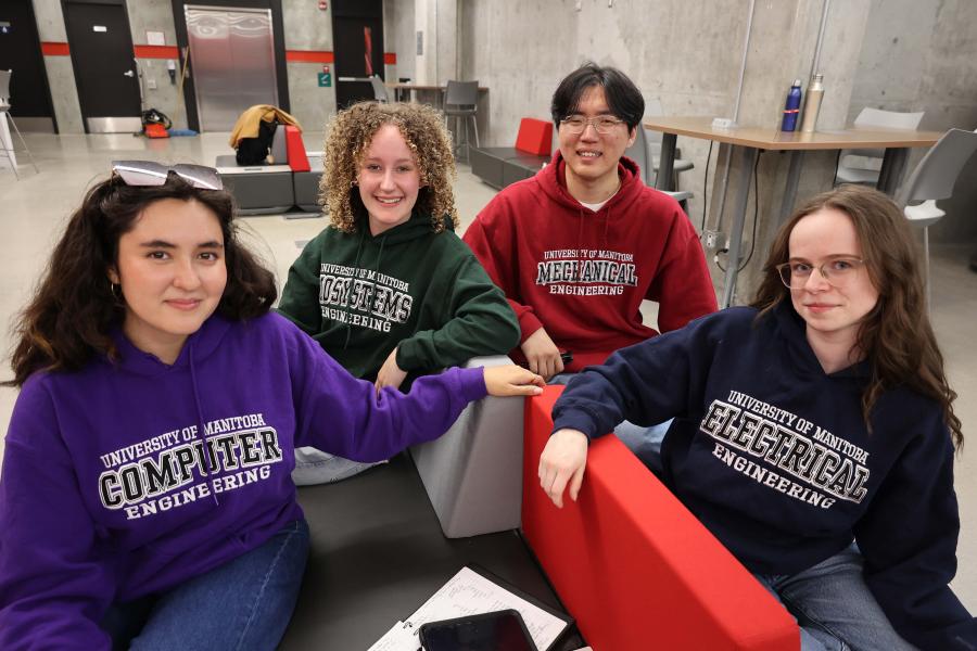 four students smiling at camera in an indoor study lounge wearing branded departmental sweatshirts