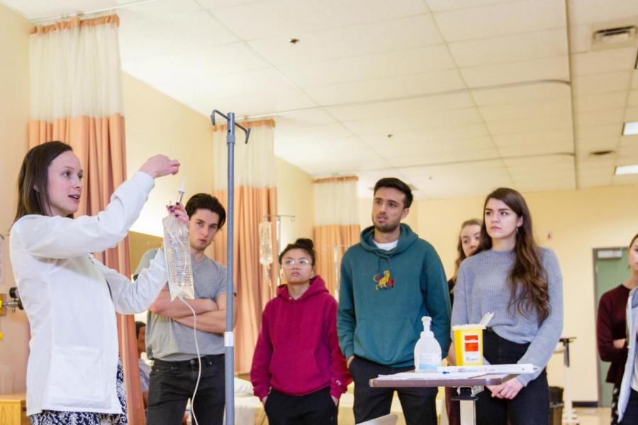 Students observe an instructor hanging an intravenous bag.